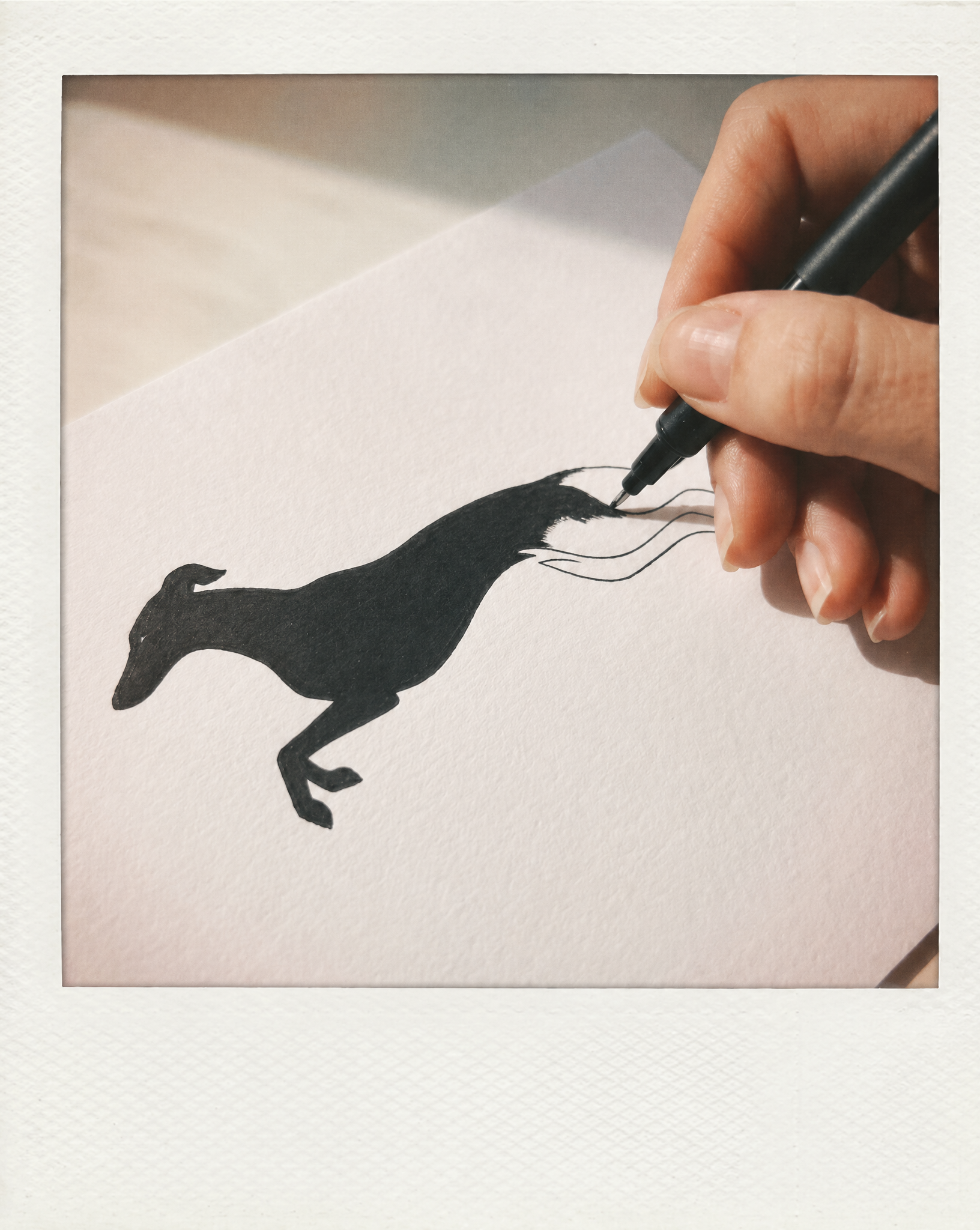 Hand drawing a black silhouette of a galgo on white paper with a pen.